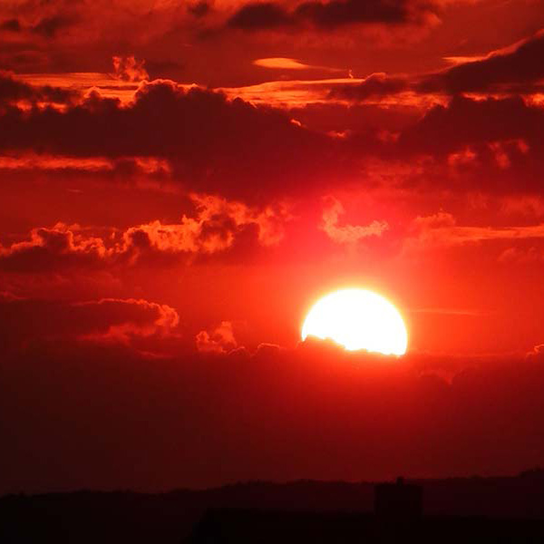 red, maroon, and dark orange clouds with the white sun behind