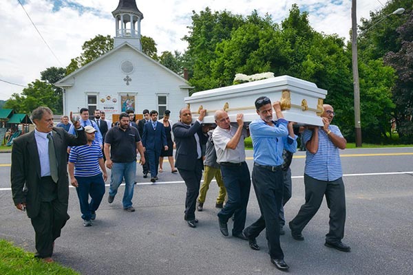 men carry a white casket across a road in a Coptic funeral procession