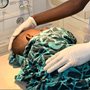 man in blue doctors scrubs caring for a baby wrapped in blue and black African fabric