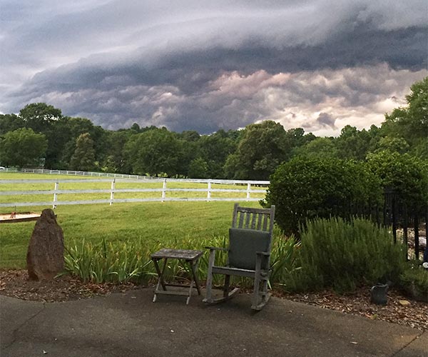 photo of a rocking chair on a front porch with a white fenced field in the background