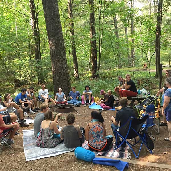 group of people sitting in a circle in a forest clearing