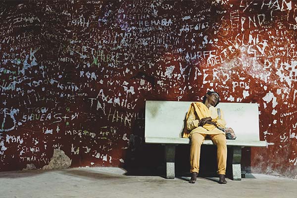 woman in yellow clothes sleeping on a bench against a wall filled with graffiti 