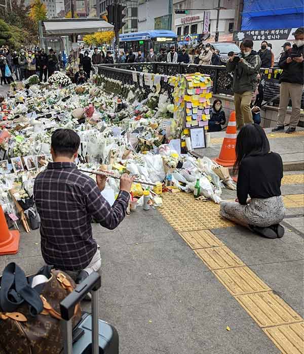 man playing flute in front of a pile of flowers