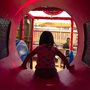 child playing in fast food restaurant playground with her mom in the background