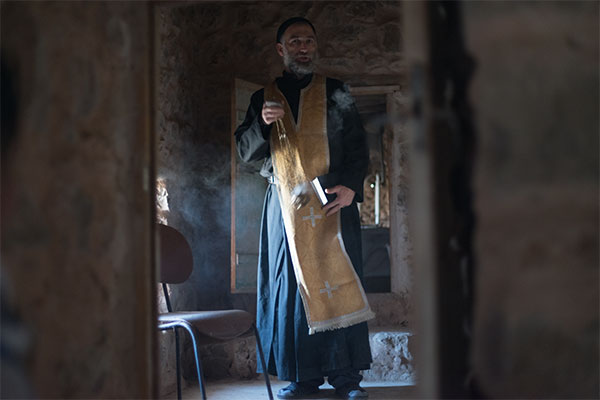 man in robes standing in a sunlit room with a censor of incense