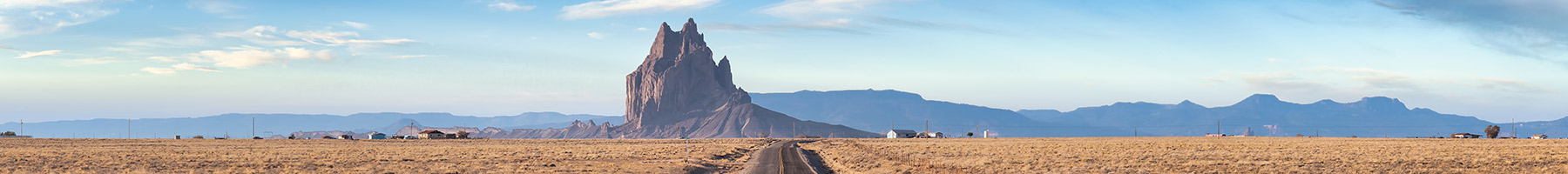 road in a dry desert with a Shiprock mountain peak in the background