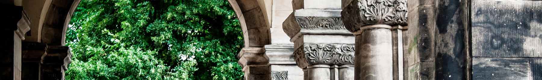 Image of large gray stone arches with green leaves at the end of the path