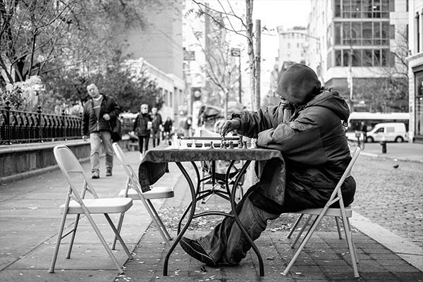 An elderly man playing chess by himself on a New York City street.