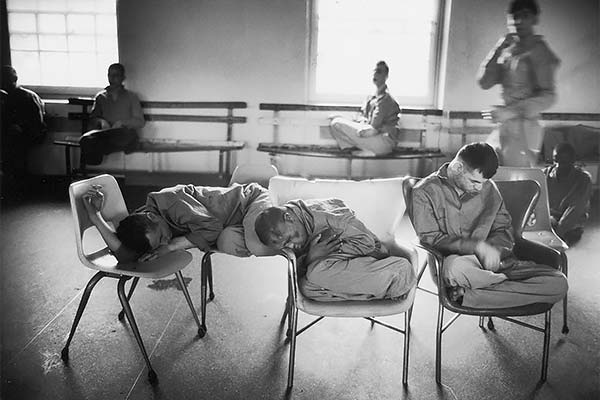 black and white photo of several men in pajamas sleeping in metal chairs