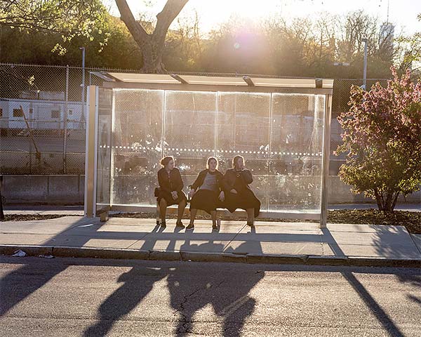 three girls sitting in a bus stop shelter in sunlight