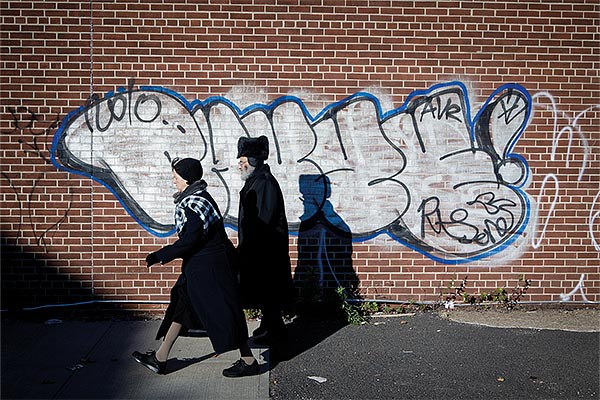 Hasidic man and woman walking past graffiti on a brick wall