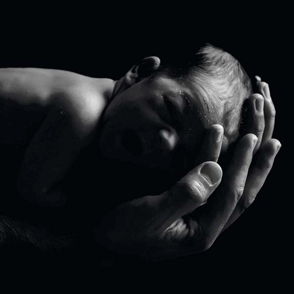 black and white photo of a mans hands holding a newborn baby