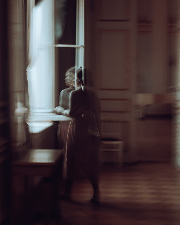 photograph of a woman standing by an open window