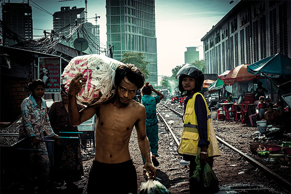 skinny man carrying a bag over his shoulder in a poor neighborhood