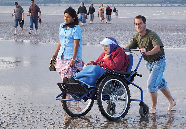 elderly person being pushed in a wheelchair by the beach